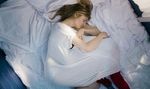 24 Wochen schwangere Frau, ganz in weiss liegt in Embryonalhaltung auf weisssem Bett auf einem Bett